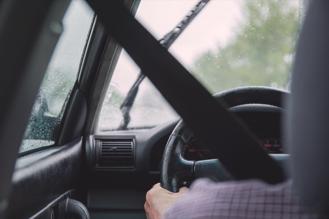 View from the driver seat through a rain-flecked windscreen with the seatbelt across the frame