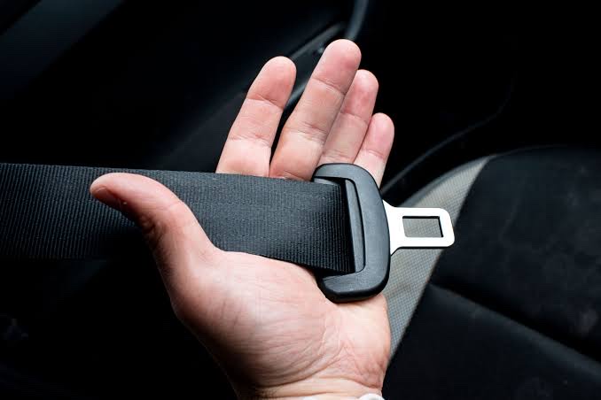 An open palm holding a black seatbelt webbing and its metal tongue