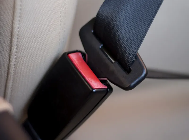 A seatbelt buckle with a red release button mounted beside a light fabric vehicle seat