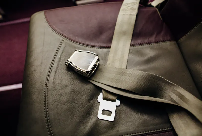 A lap-style seatbelt with a metal latch plate lying across an olive leather seat