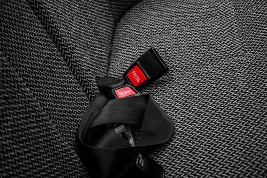 A black seatbelt buckle with a red release button set against dark herringbone upholstery