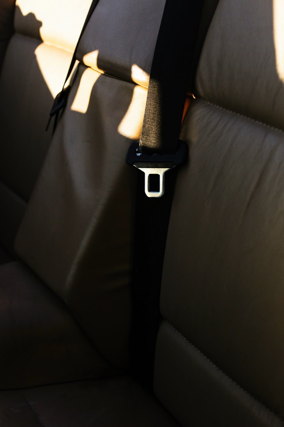 A dark seatbelt across a leather rear seat lit by angled daylight
